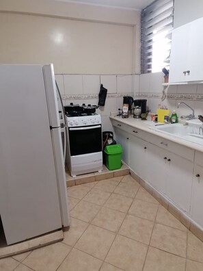 Une cuisine avec un réfrigérateur, une cuisinière et un four blancs, une poubelle verte et un plan de travail sur lequel se trouvent divers objets.