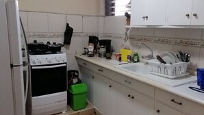 A kitchen with white cabinets, a stove, a sink, and a window with blinds.
