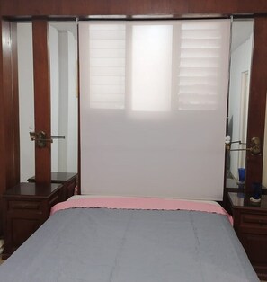 Une chambre à coucher avec un lit, une commode, un miroir et une fenêtre avec des stores.