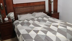 A bedroom with a wooden headboard, a bed with a geometric patterned bedspread, a nightstand, a bedside table, and a mirror.