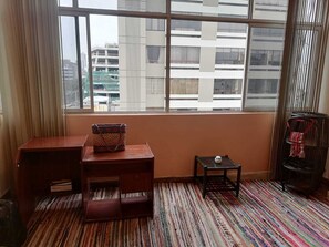 Une pièce avec une grande fenêtre, un bureau en bois, une petite table sur laquelle se trouve une balle, et un tapis rayé aux couleurs vives.
