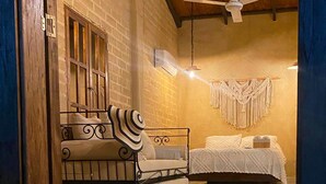 Een slaapkamer met een bed, een bank, een plafondventilator en een macramé wanddecoratie.