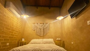 Een kamer met een bed, een macramé wanddecoratie en een aan de muur bevestigde televisie.