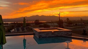 A swimming pool with a stone structure in the center, surrounded by a poolside area with umbrellas. - The Perfect Lake Havasu Lake View Pool/Spa Home getaway!!! (Lake Havasu City)