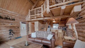 L’intérieur d’une cabane en rondins, avec un escalier en bois, un canapé en cuir, une table à manger et un télescope.