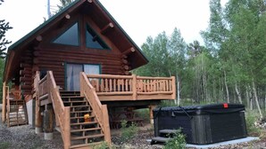Une cabane en rondins avec une terrasse en bois et un jacuzzi.