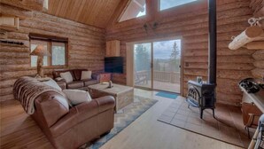 L'intérieur d'une cabane en rondins, avec un canapé en cuir, une cheminée et une grande fenêtre.
