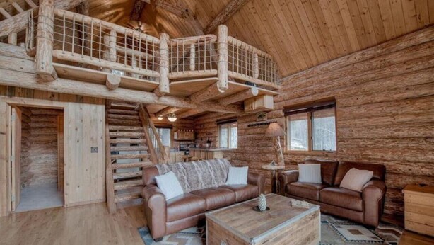L’intérieur d’une cabane en rondins, avec un escalier en bois, des canapés en cuir et une table basse en bois.