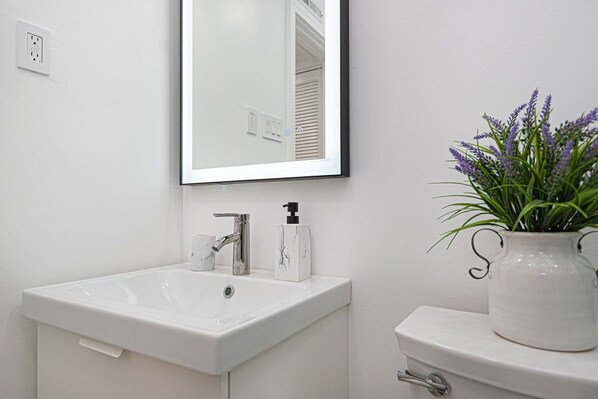 A bathroom with a white sink, a mirror, and a toilet. There is a potted plant on the toilet.