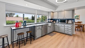 Une cuisine moderne avec des meubles gris, une grande fenêtre et un coin repas doté de chaises en bois.