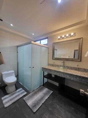 Un baño moderno con cabina de ducha de vidrio, un espejo grande y encimera de granito.