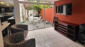 Ein modernes Wohnzimmer mit an der Wand montiertem Fernseher, einer Couch und einem Essbereich inklusive Tisch und Stühlen.