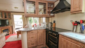 A compact kitchen with wooden cabinets, a black stove, and a countertop with kitchen utensils. - 10 Old Orchard (Much Wenlock)
