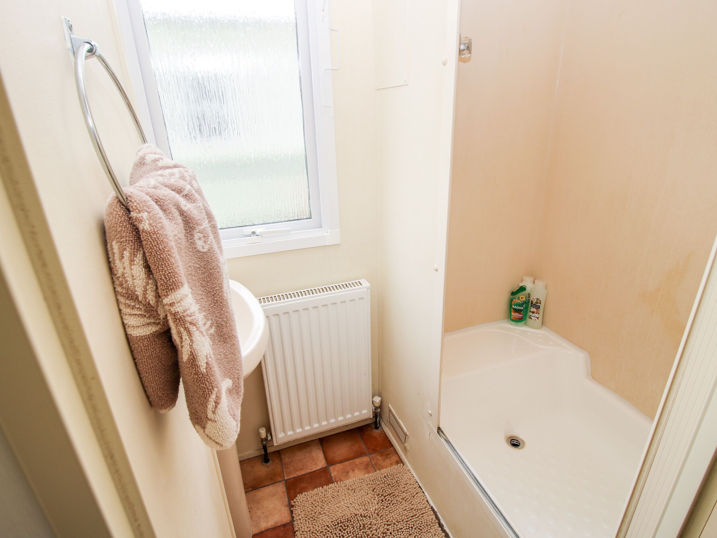 A bathroom with a white sink, a towel rack, a window, a radiator, and a shower area.
