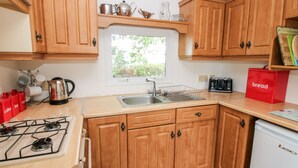 A compact kitchen with wooden cabinets, a gas stove, a sink, and a window providing natural light. - 6 Old Orchard (Much Wenlock)