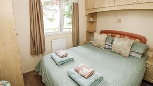 A bedroom with a bed, a window with curtains, a radiator, and wooden cabinets. - 6 Old Orchard (Much Wenlock)