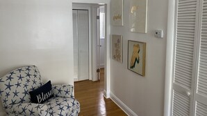 En hall med en mönstrad fåtölj, en dörr med lamellluckor och flera konstverk som hänger på väggen.