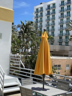 A balcony with a yellow umbrella, white railings, and a view of a multi-story building with balconies. - Beautifully Remodeled Condo on Hollywood Boardwalk (Hollywood)