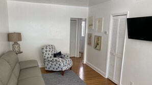 Ett vardagsrum med en soffa, en mönstrad fåtölj, en lampa och konstverk på väggarna.