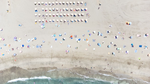 Een luchtbeeld van een strand met veel parasols en mensen.