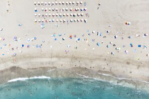 Vista aérea de una playa con numerosas sombrillas y gente.