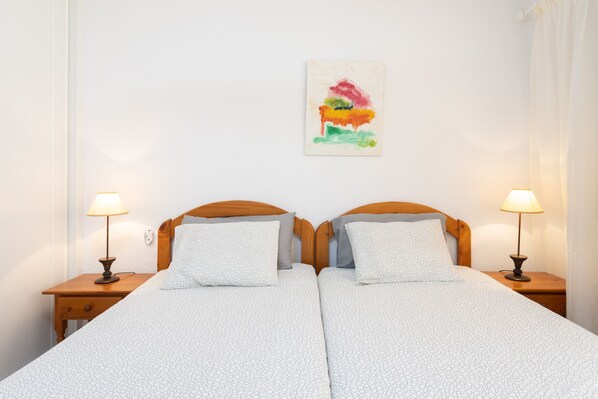 Una cama doble con colcha estampada, dos mesitas de noche con lámparas y un cuadro abstracto colorido en la pared.