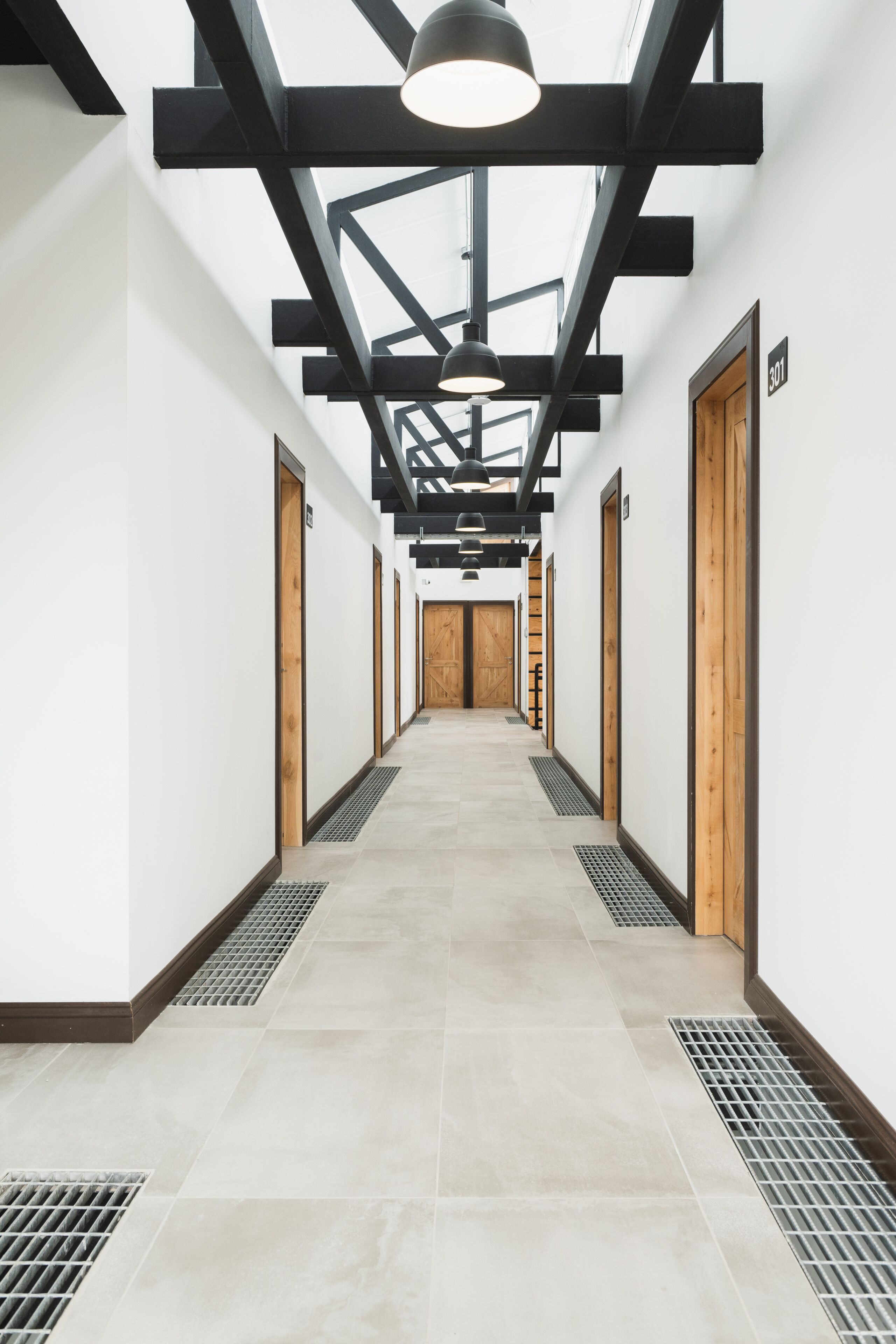 A modern hallway with a high ceiling, black beams, and a series of wooden doors.