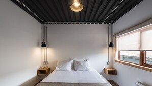 Un dormitorio con una cama, dos mesitas de noche, una ventana y una lámpara en el techo.
