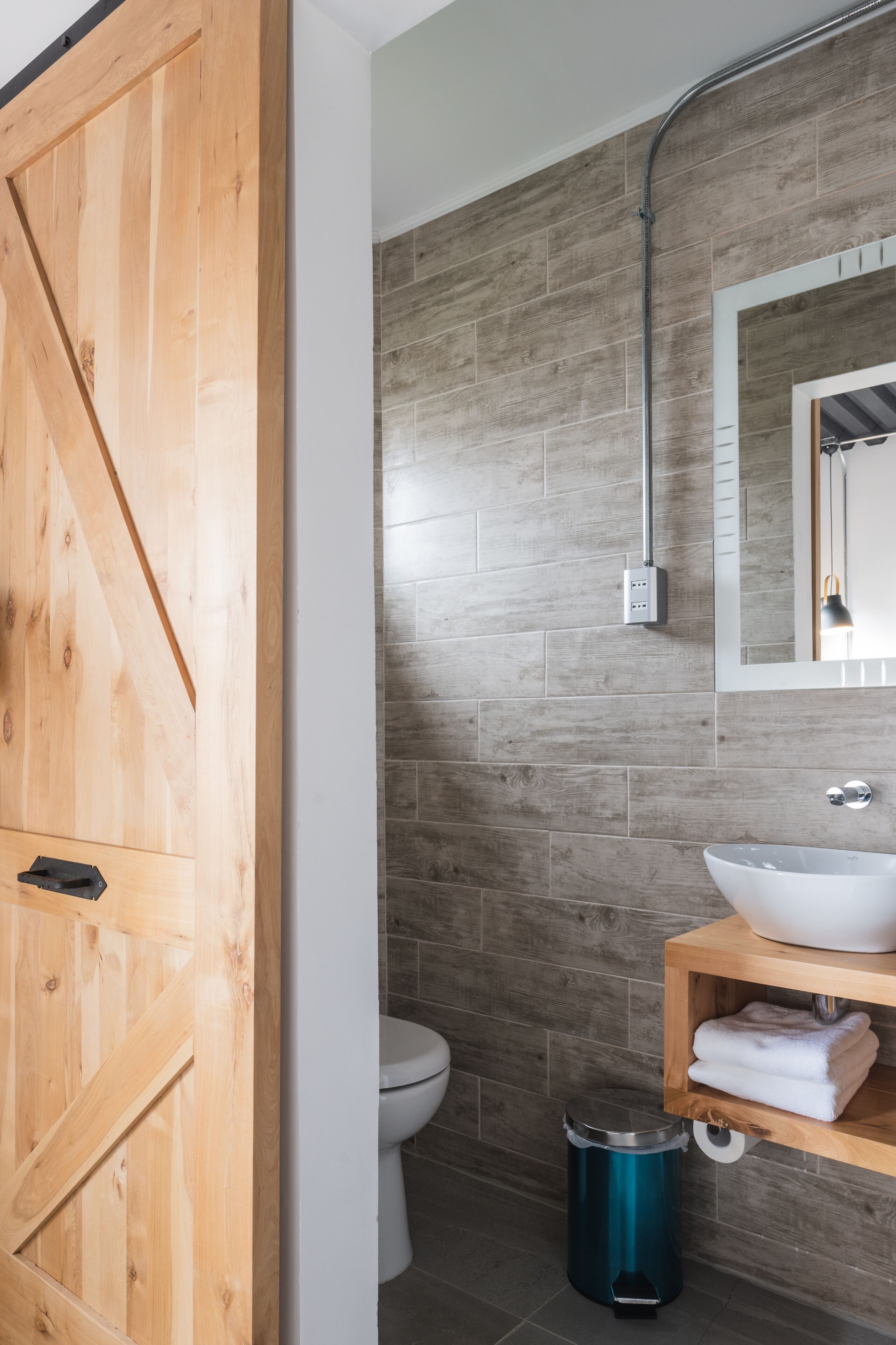 Un baño con una puerta de madera, un lavabo blanco, un espejo y un inodoro.