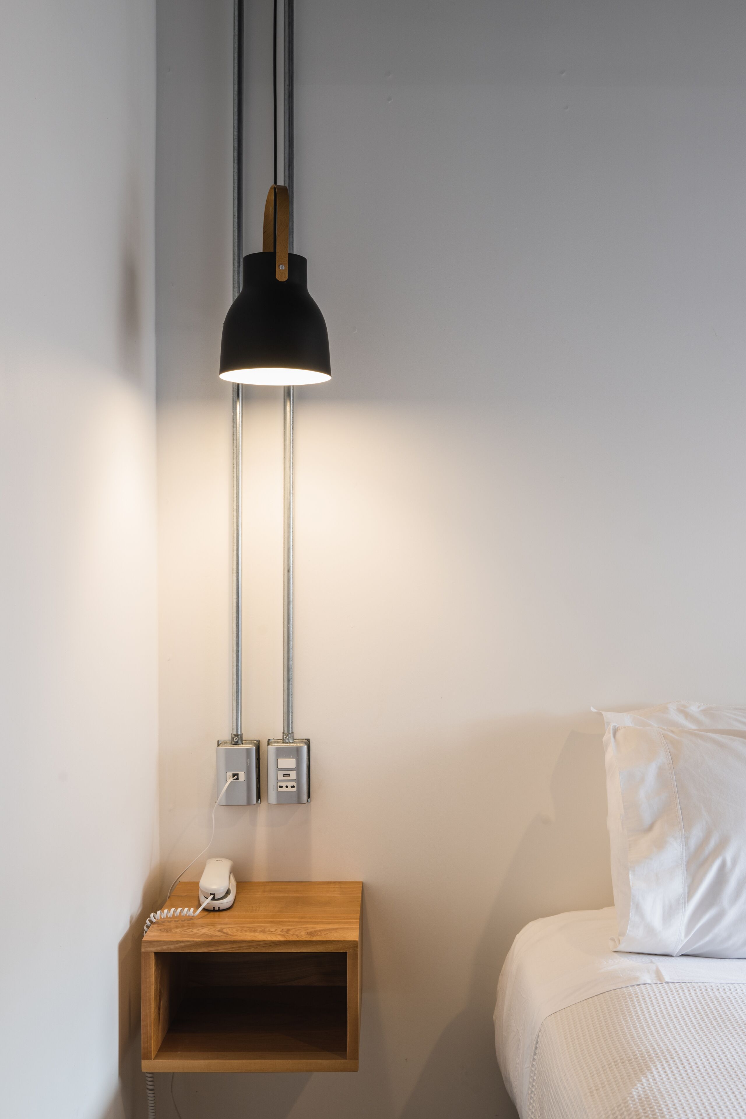 A modern bedroom with a bed, a bedside table with a phone, and a pendant light fixture.