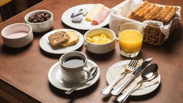 Uma mesa de madeira com café, torradas, ovos mexidos, presunto, queijo e um copo de suco de laranja.
