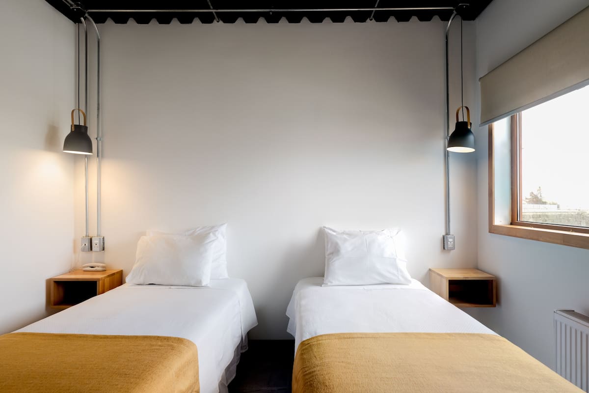 A twin room with two beds, bedside tables, lamps, a window with a view, and a radiator.