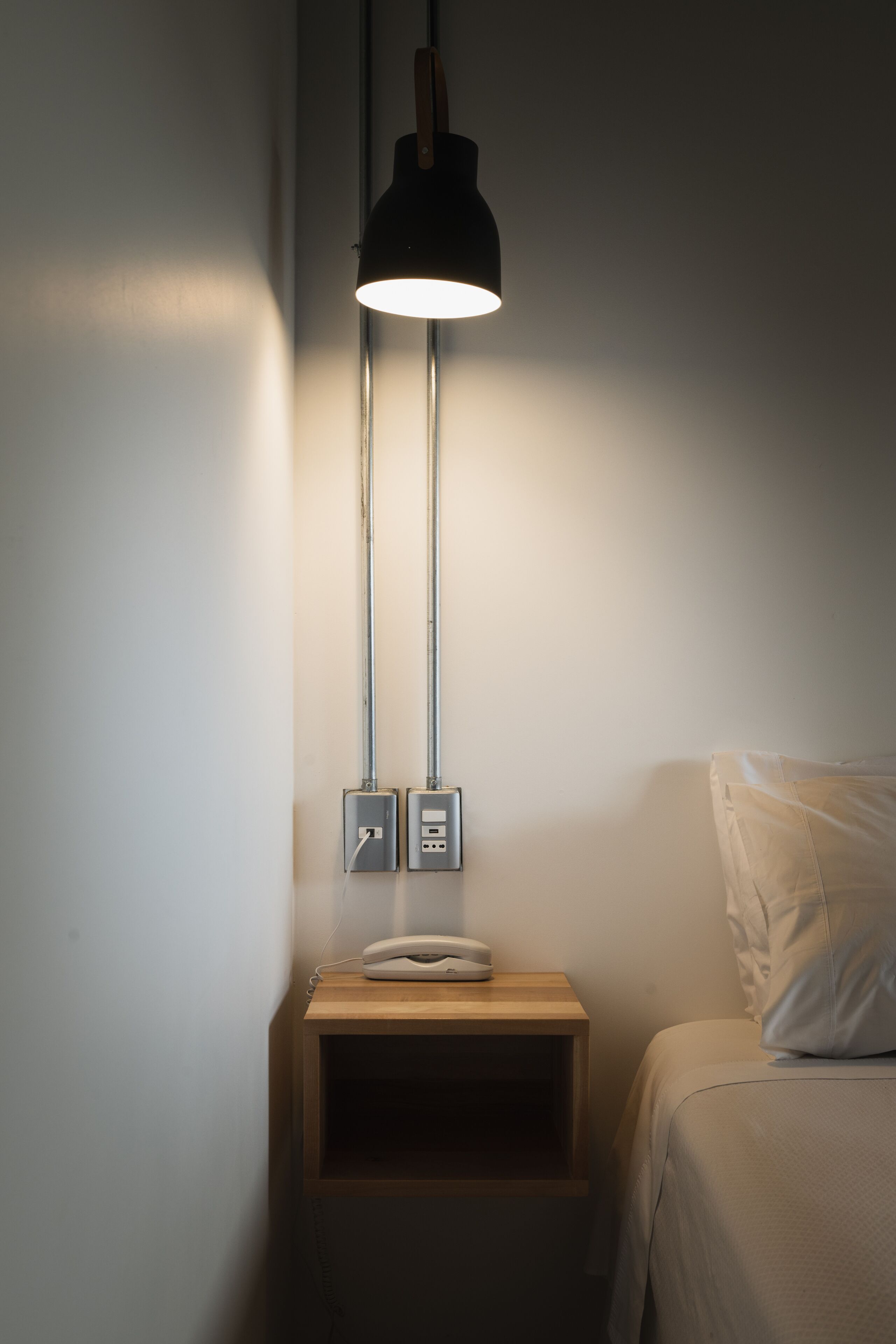 A bedside table with a lamp, a phone, and a power outlet.