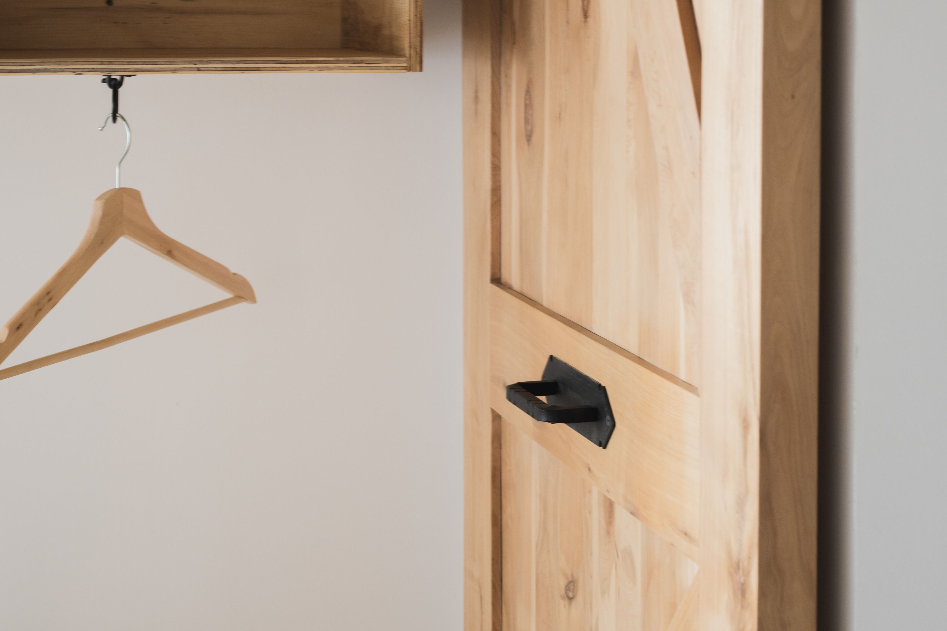 A wooden wardrobe with a black handle and a wooden hanger on the wall.