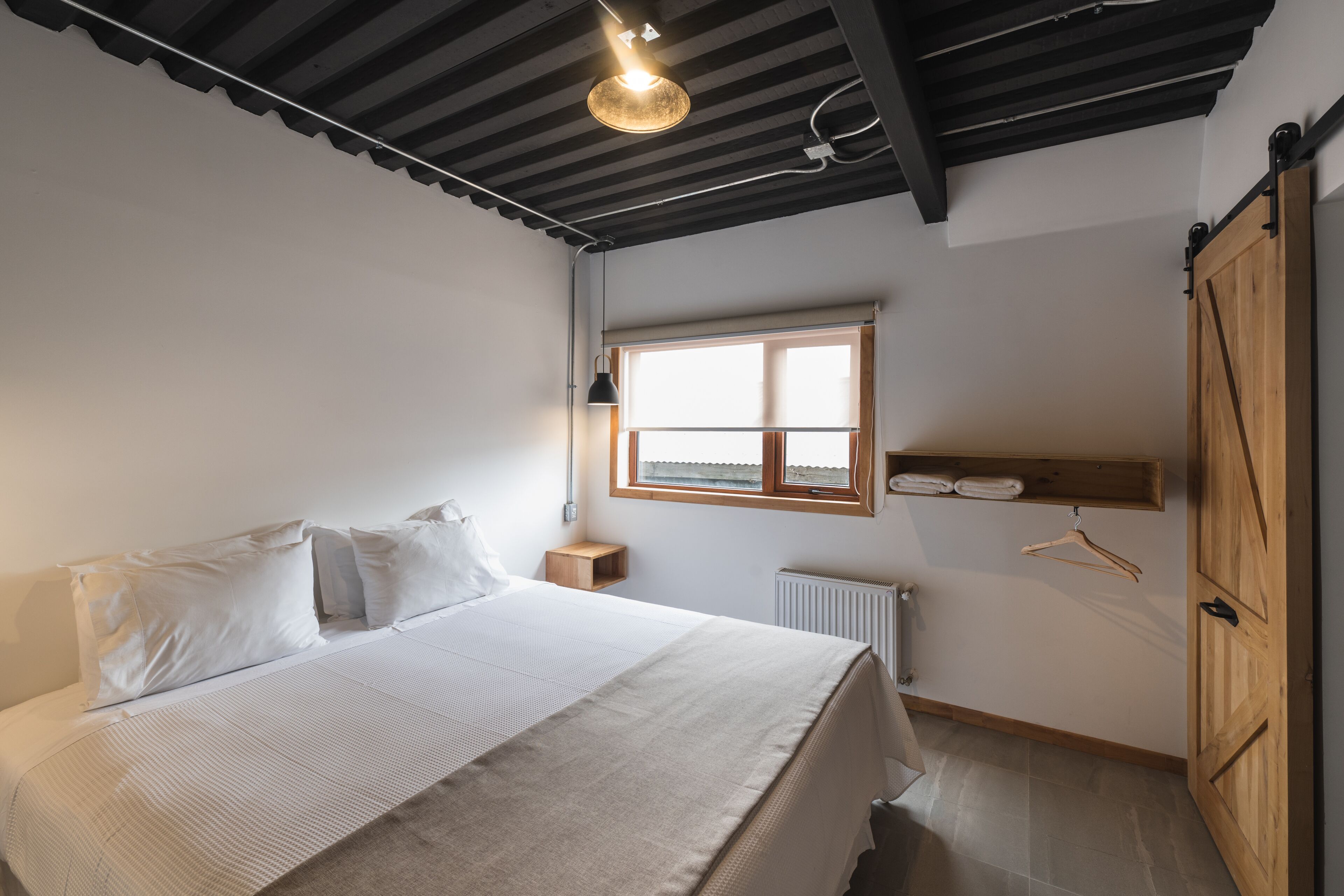 A bedroom with a bed, a window, a radiator, and a wooden wardrobe.