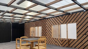 Un espacio interior con una mesa y sillas de madera, un panel negro y una pared con diseño en chevron.
