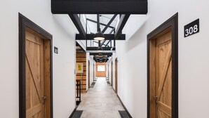Un pasillo con puertas de madera, con los números 307 y 308, que conduce a una habitación con piso de madera y un tragaluz.