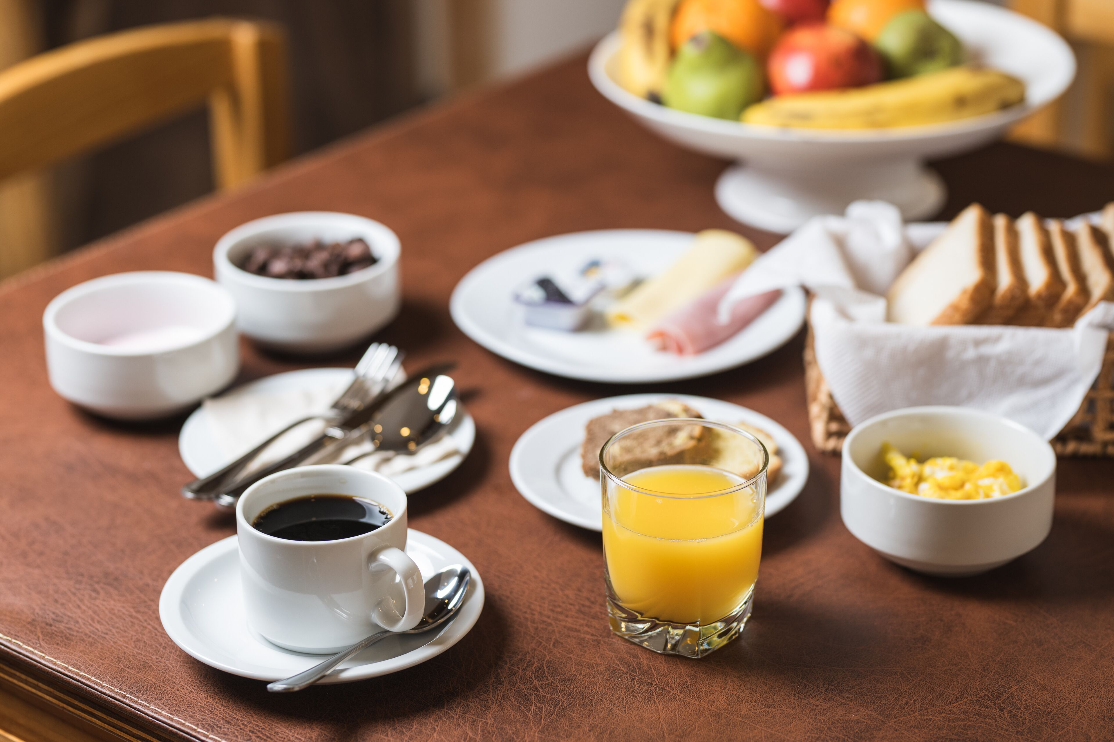 Una mesa de desayuno con café, zumo de naranja, huevos revueltos, tostadas y un bol de fruta.