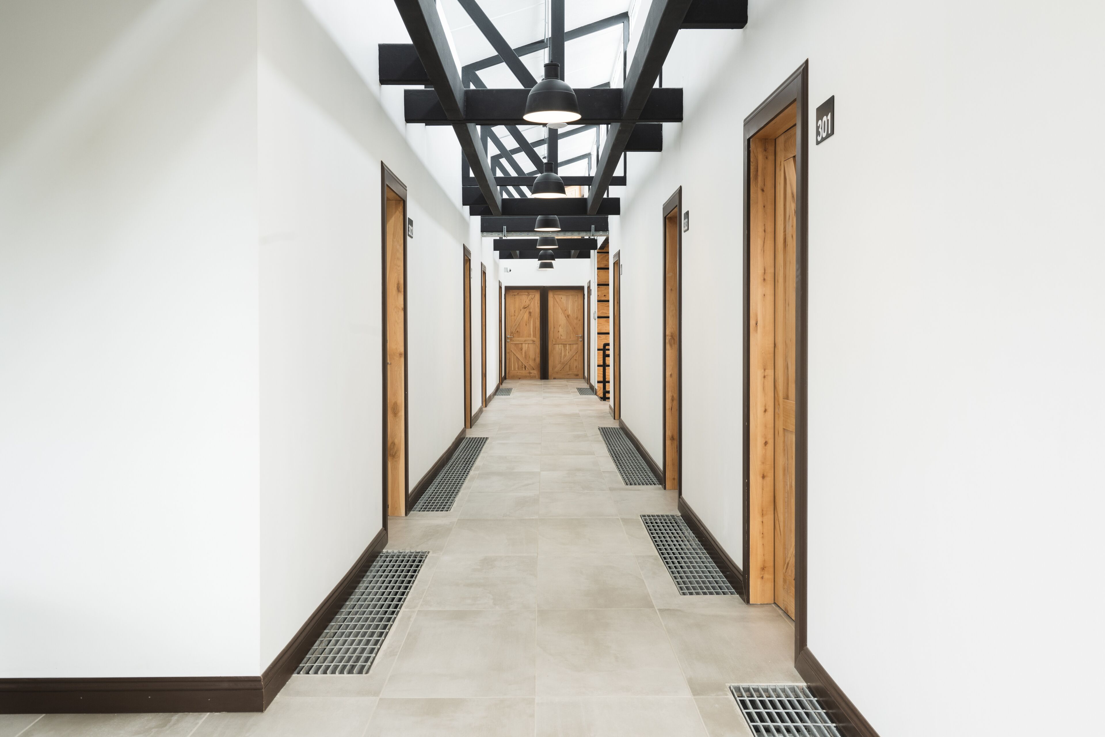 A modern hallway with a high ceiling, wooden doors, and a tiled floor.