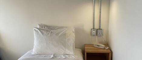 A single bed with white bedding, a bedside table with a telephone, and a wall-mounted light fixture.