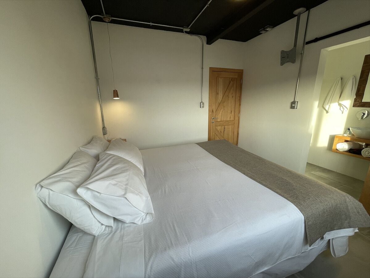 A bedroom with a bed, a wooden door, a towel rack, and a small table with a mirror.