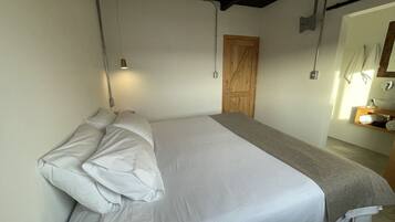 A bedroom with a bed, a wooden door, a towel rack, and a small table with a mirror.