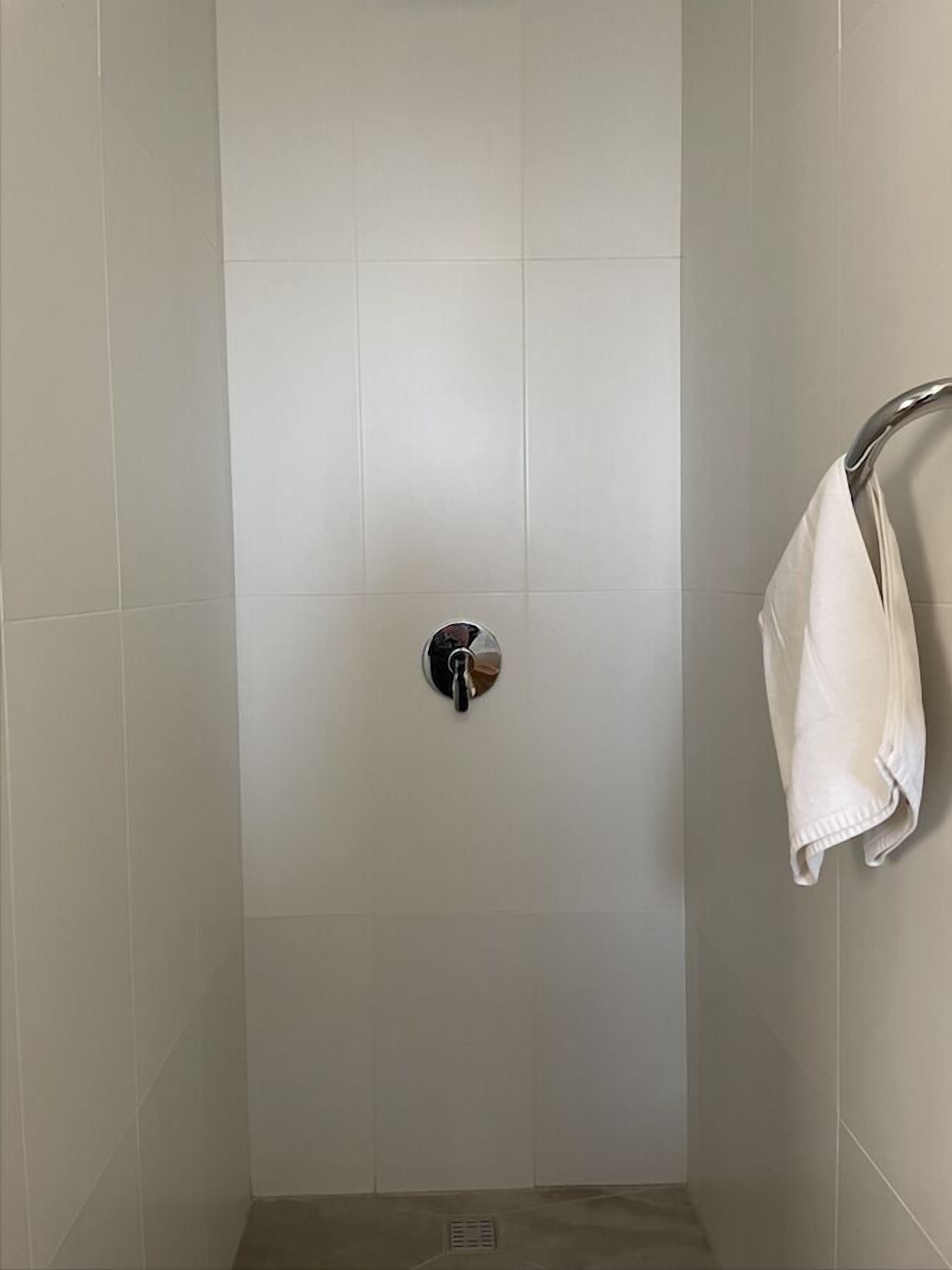 A shower with a chrome faucet and a towel rack with a white towel.