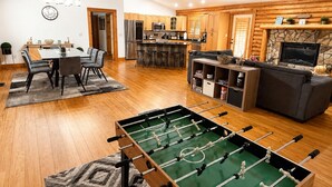 Una cucina moderna con mobili in legno, un'area pranzo con tavolo e sedie, un soggiorno con divano e camino, e un tavolo da calcio da tavolo.