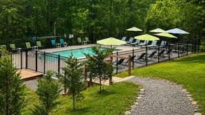 Una piscina con lettini e ombrelloni, circondata da un recinto e alberi.