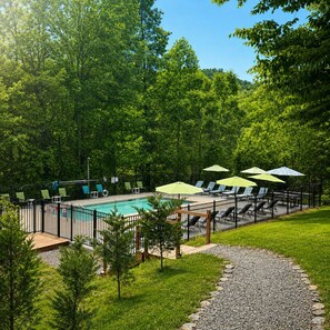 A swimming pool with lounge chairs and umbrellas, surrounded by a fence and trees.