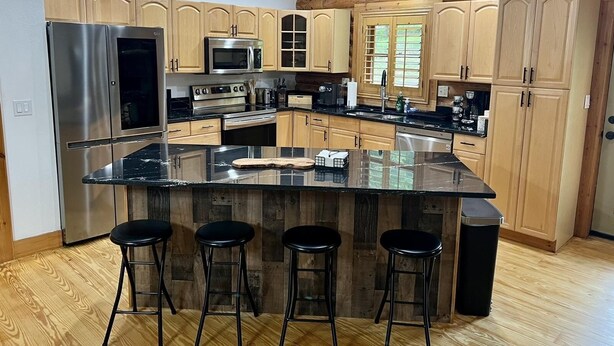 Una cucina moderna con mobili in legno, elettrodomestici in acciaio inossidabile, un'isola centrale con sgabelli e una finestra con persiane.