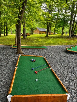 A pool table with balls and cues, surrounded by trees and a grassy area.