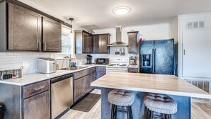 Una cocina moderna con armarios de madera oscura, una isla central con taburetes, un refrigerador de acero inoxidable y un horno empotrado.