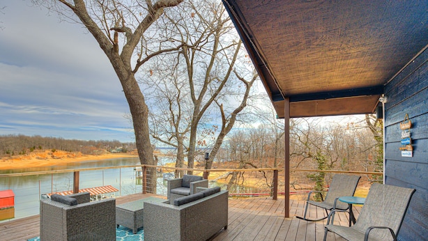 Una terraza de madera con muebles de mimbre, vista a un río y un área cubierta con un letrero.